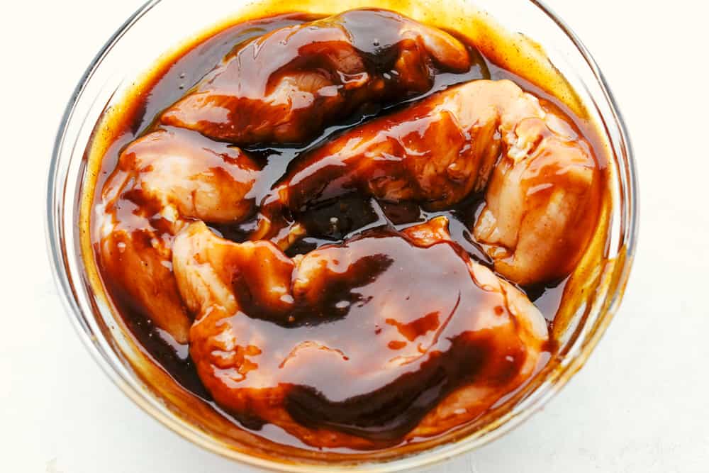 Chicken marinating in barbecue sauce in a glass bowl.