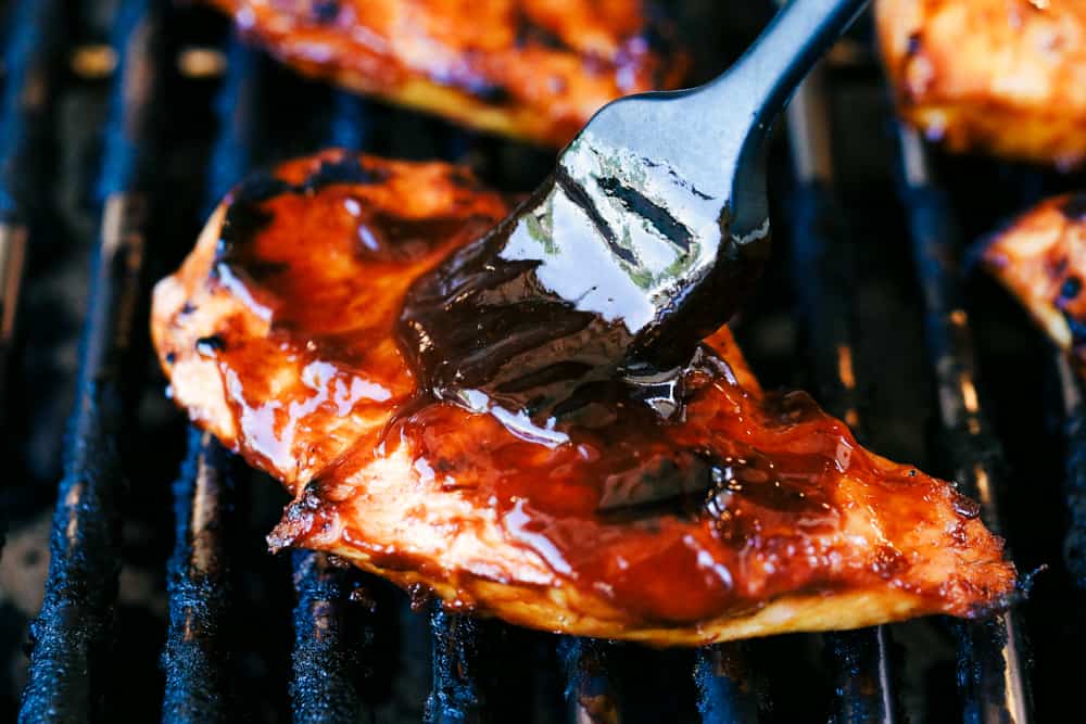 Brushing barbecue sauce on chicken while it is grilling.