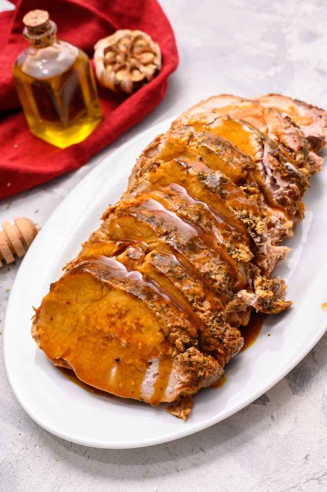 Slow cooker parmesan honey pork roast on a white platter sliced up. 