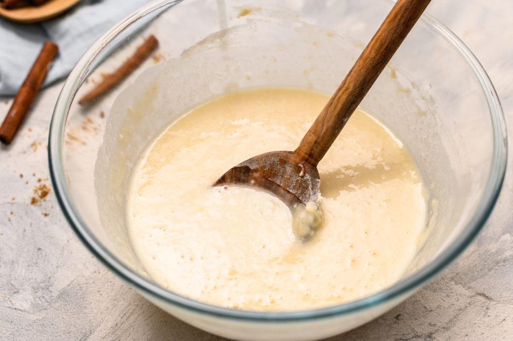 Cobbler dough mix being stirred by a wooden spoon in a glass bowl. 