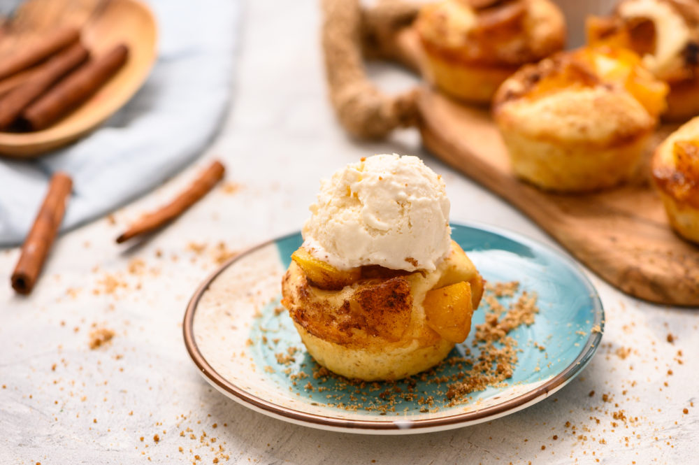 Mini peach cobbler on a plate with cinnamon sticks around and the mini peach cobbler topped with a scoop of vanilla ice cream. 