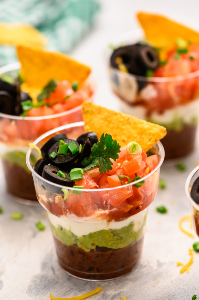 Individual cups with seven layers of refried beans, guacamole, sour cream and topped with tomatoes, black olives, scallions and a chip.