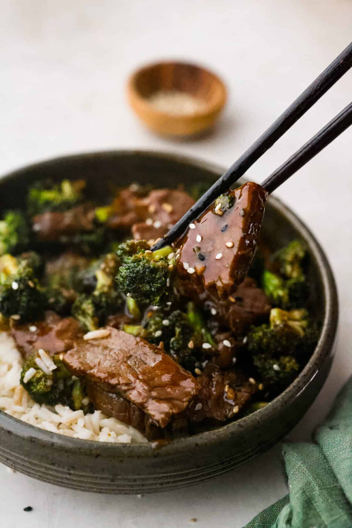 Side shot of someone taking a bit of Mongolian beef and broccoli with chop sticks from a plated dish. 