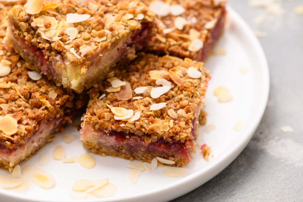 Raspberry cheesecake bars stacked on top of each other on a white plate. 