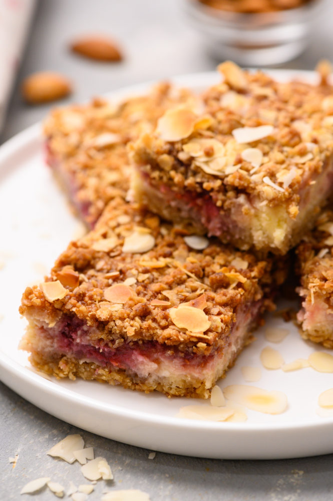 Raspberry cheesecake bars stacked on top of each other on a white plate. 