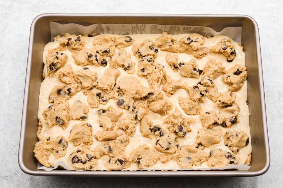 Overhead shot of crumbles of brownie mixture on top of the cheesecake and brownie mixture.