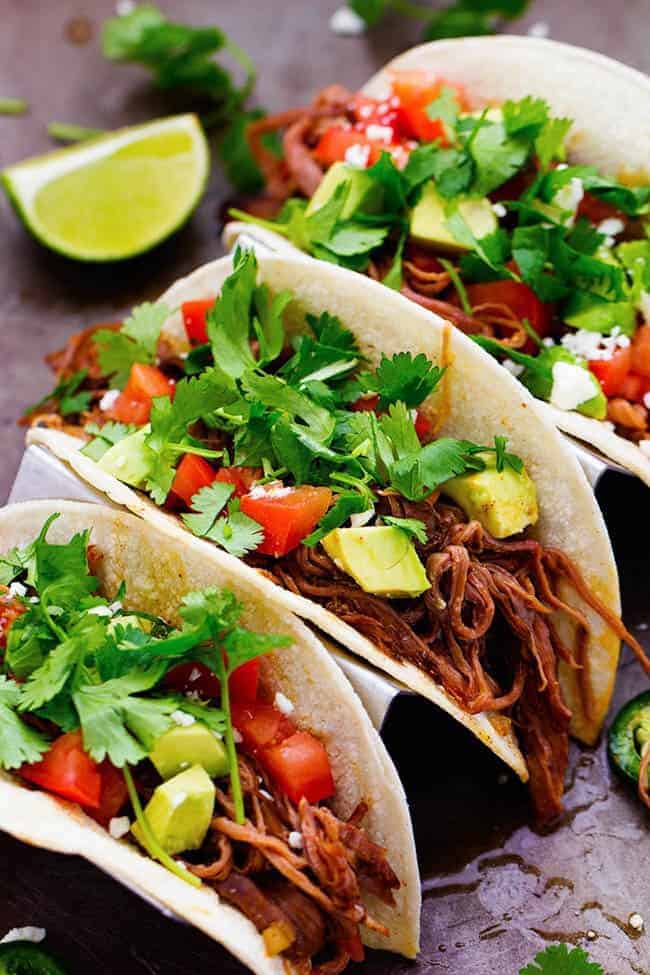 flank steak tacos with cilantro garnished on top with limes on the side. 