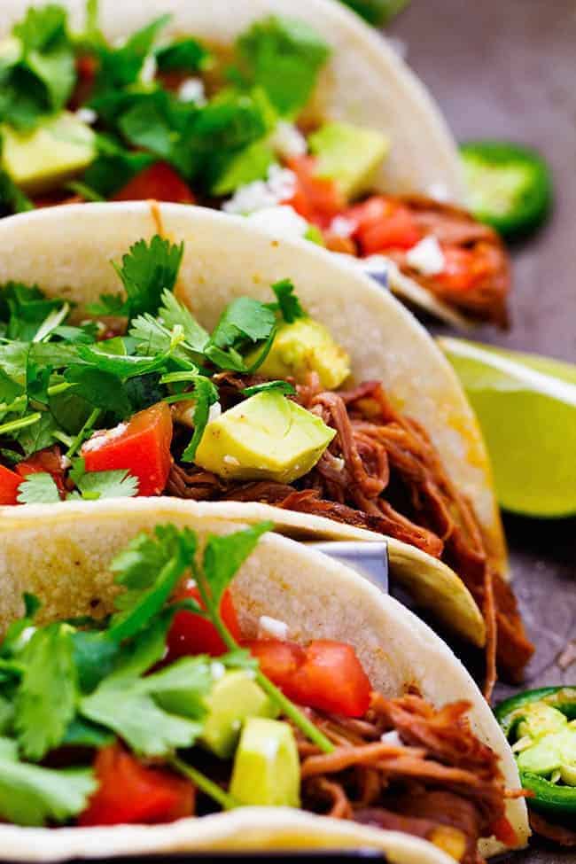 Slow cooker beef carnitas with cilantro on top and limes on the side.