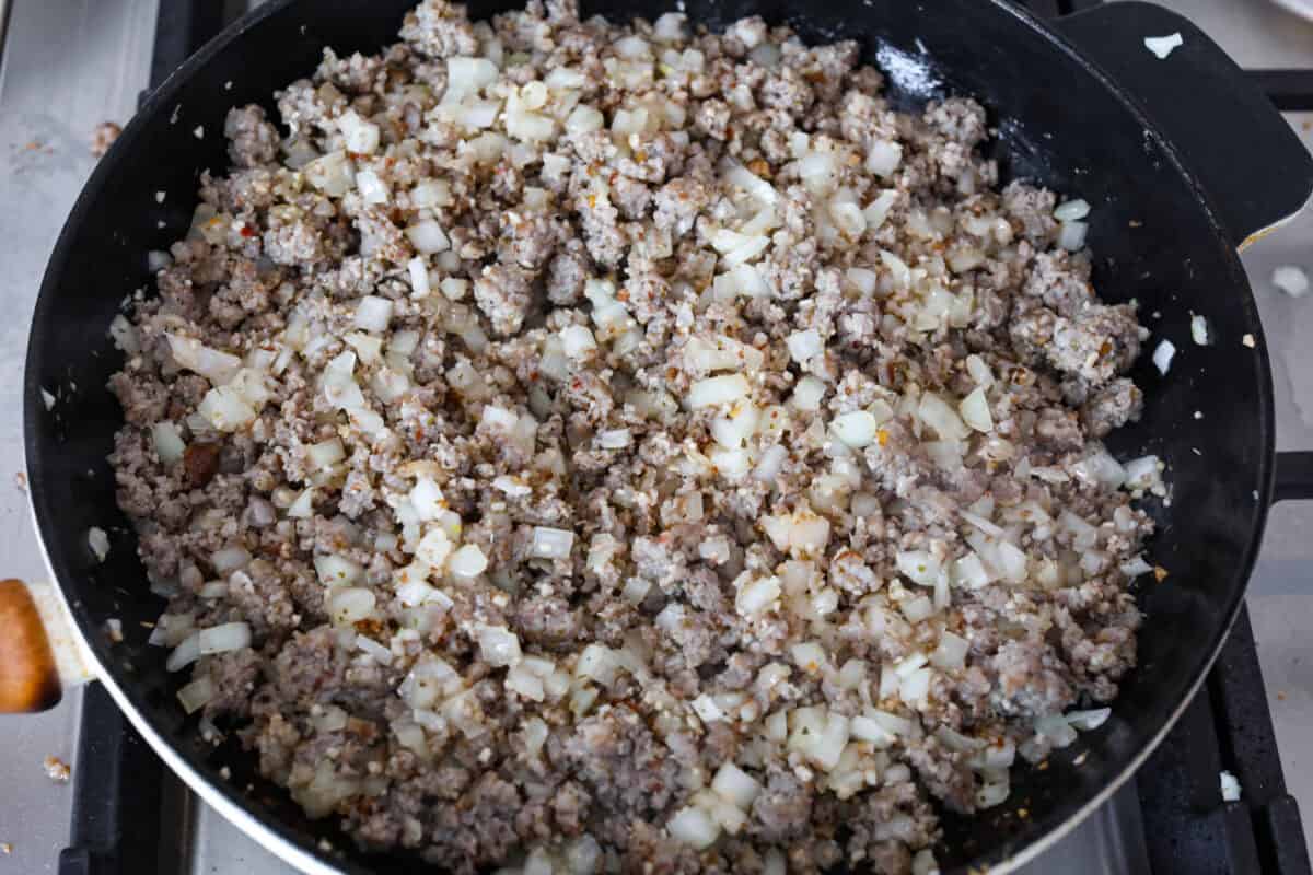 Overhead shot of pork sausage, onions and garlic being sautéed in a pan. 