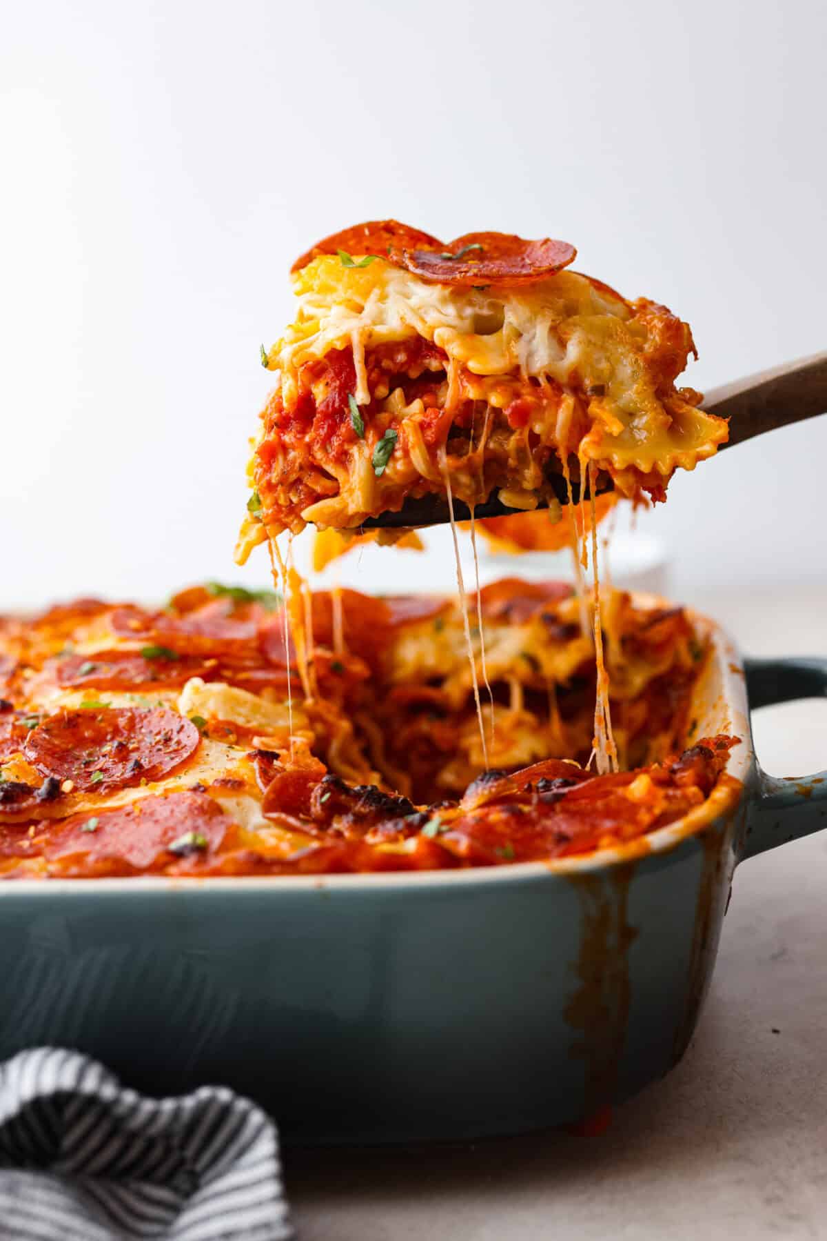 Side shot of a slice of pizza casserole being lifted out of the pan with cheesy stringiness.