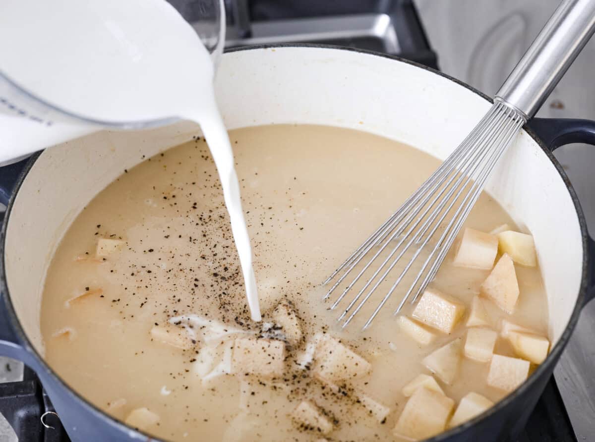 Angle shot of someone pouring the half and half into the soup mixture. 