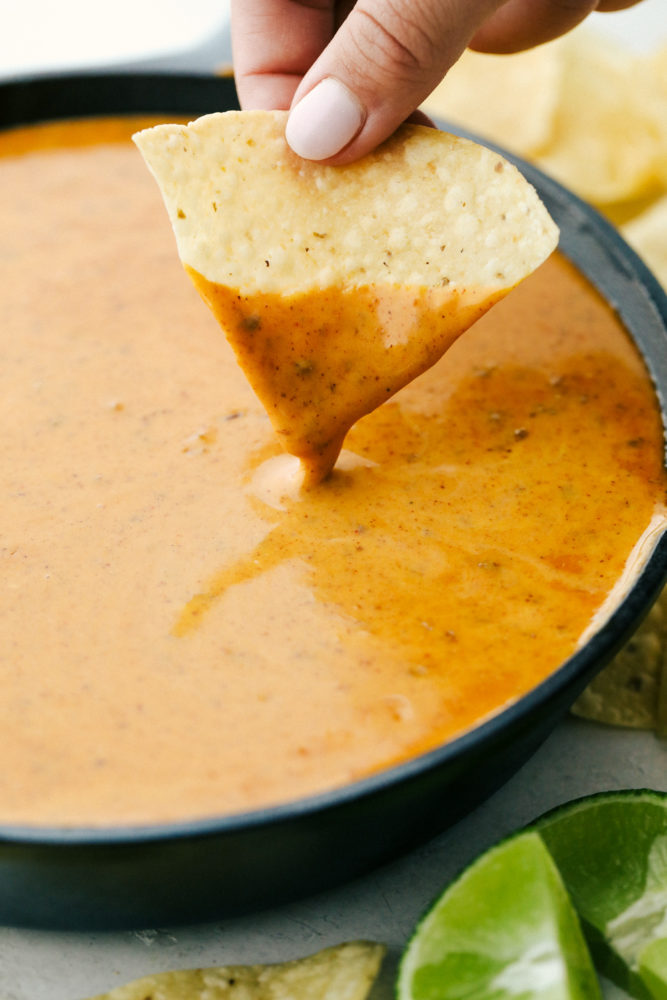 Queso in a black skillet with a chip being dipped in it. 