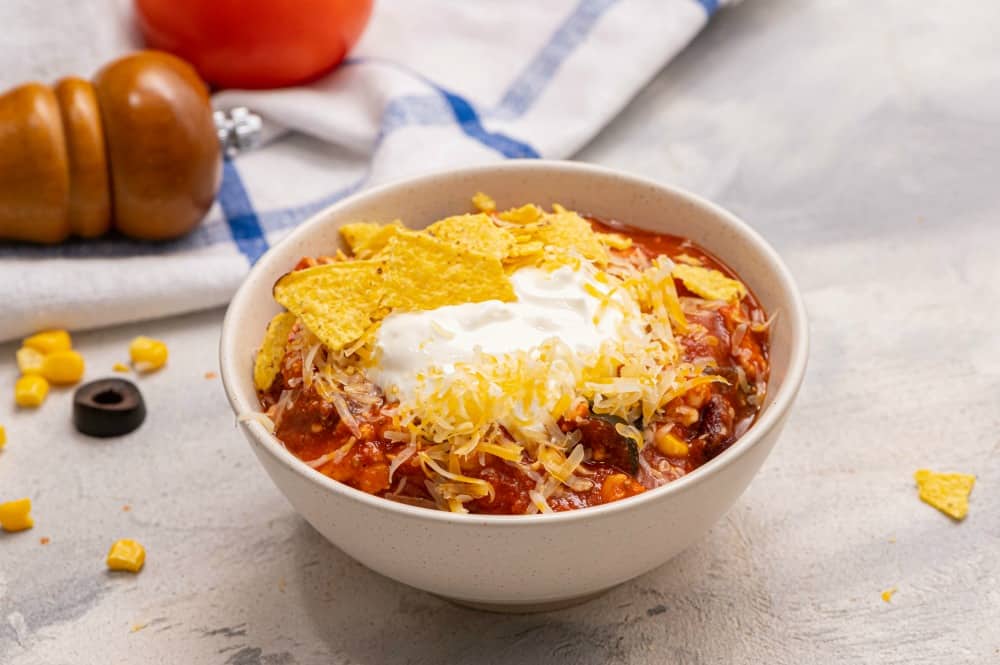 Skinny taco soup in a white bowl garnished with tortilla chips and shredded cheese. 