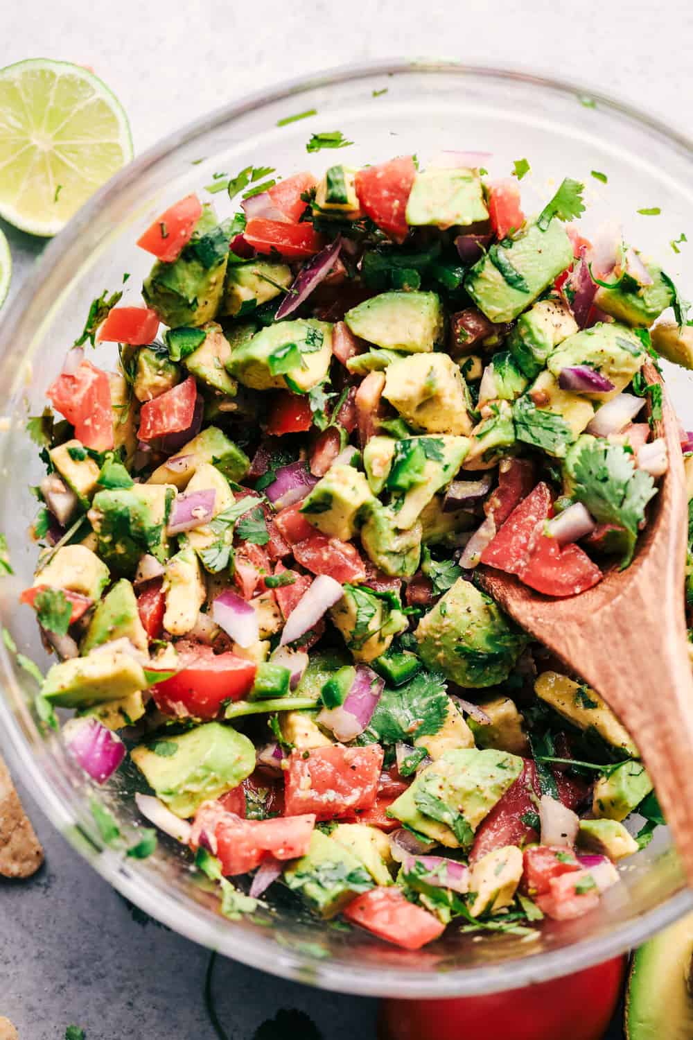 A close up photo of the california avocado dip with a wooden spoon in the mixture and a lime laying beside the bowl.