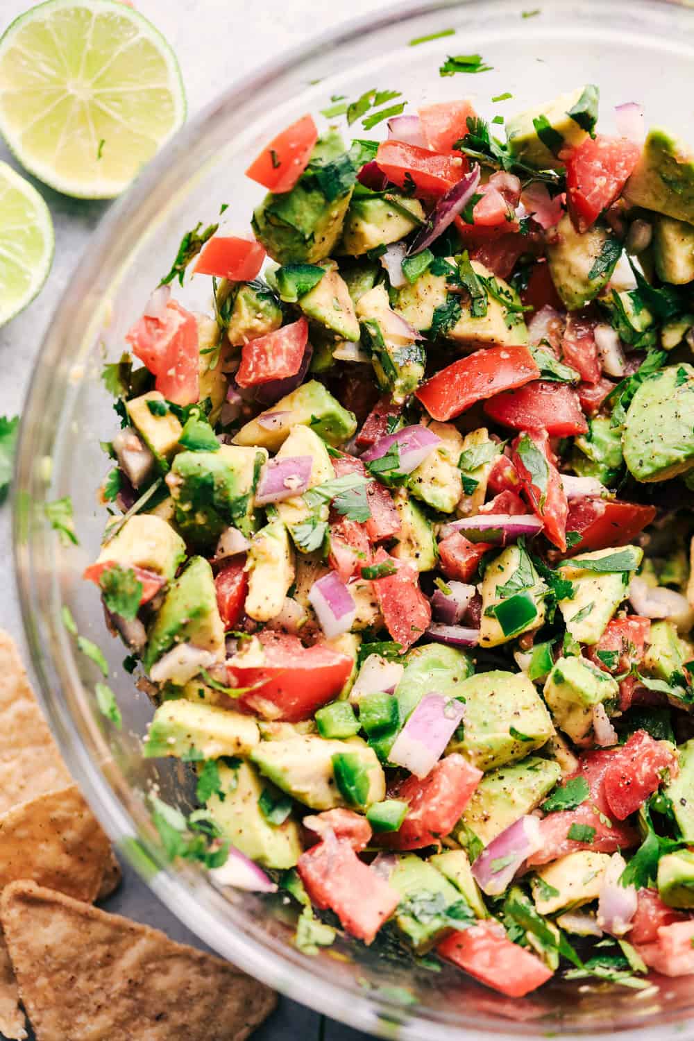 A zoomed in photo of the california avocado dip in a clear glass bowl with lime and tortilla chips sitting beside the bowl.