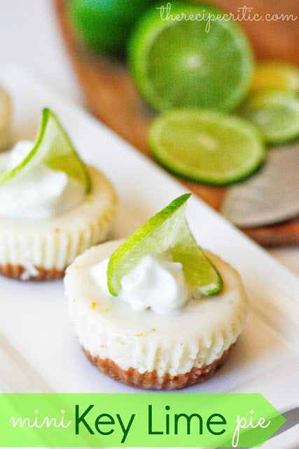 Two mini key lime pies on a white plate and garnished with a sliver of lime and a dollop of whipped cream on top. 