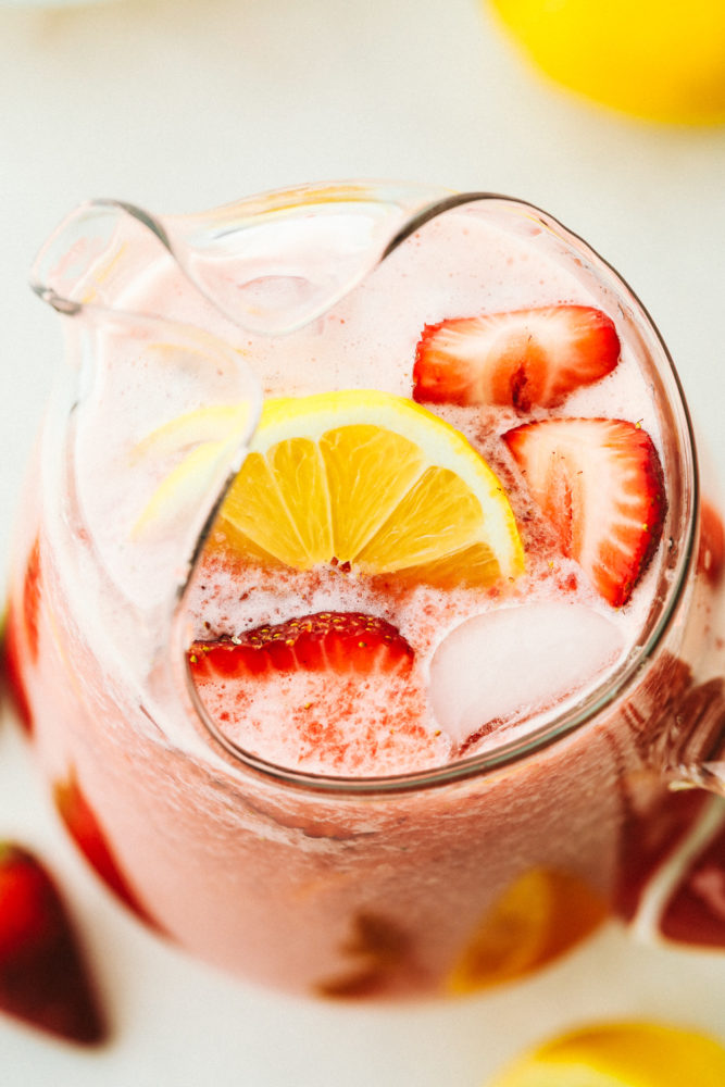 A top photo overview of a pitcher with homemade strawberry lemonade garnished with fresh cut lemons and strawberries.