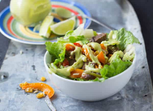 Steak fajita salad in a white bowl on a gray tray.