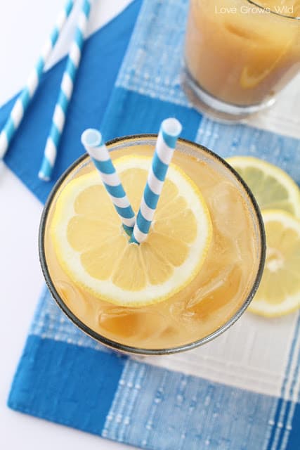 A glass of summertime tea with a lemon slice in the top and two blue and white straws.