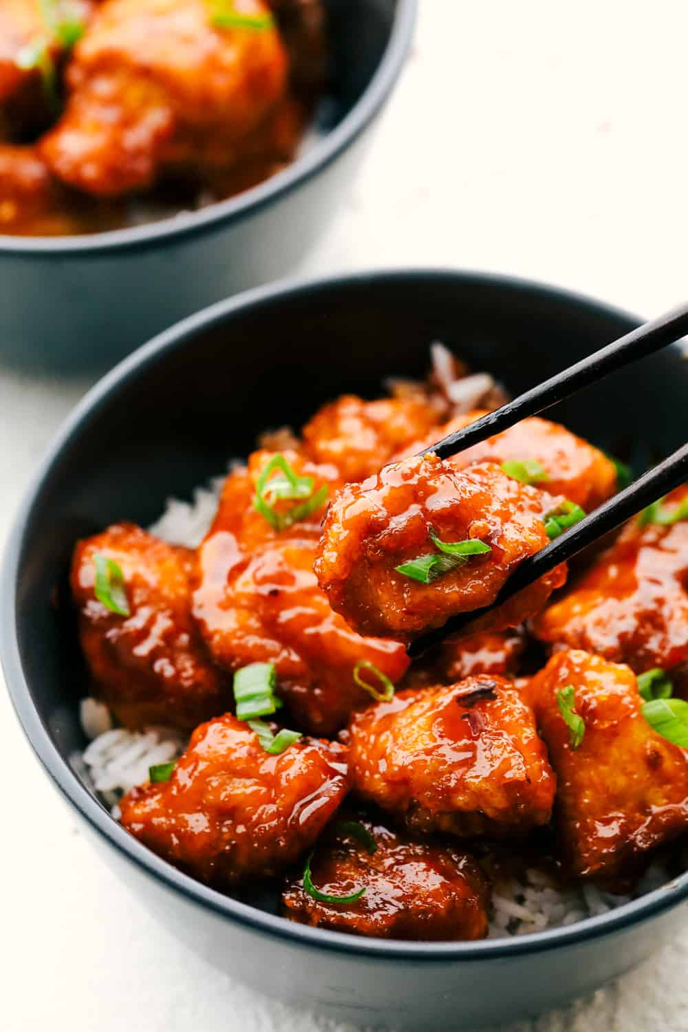 Homemade Firecracker Chicken in a black bowl over rice with some chopsticks.