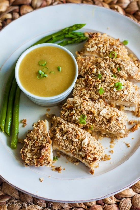 Honey Mustard Chicken cut into strips on a white plate and drizzled with honey mustard, with a side dish of honey mustard on the plate.