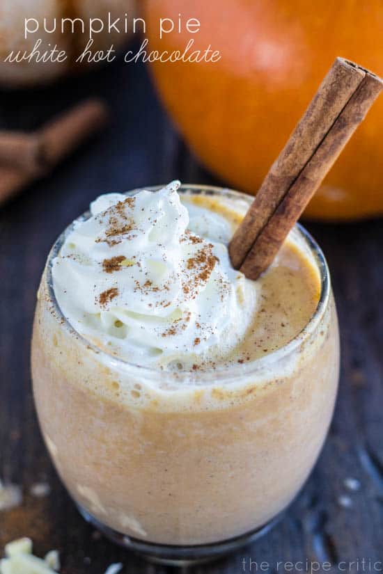 Pumpkin Pie white hot chocolate in a clear glass with whipped cream, cinnamon, and cinnamon sticks.