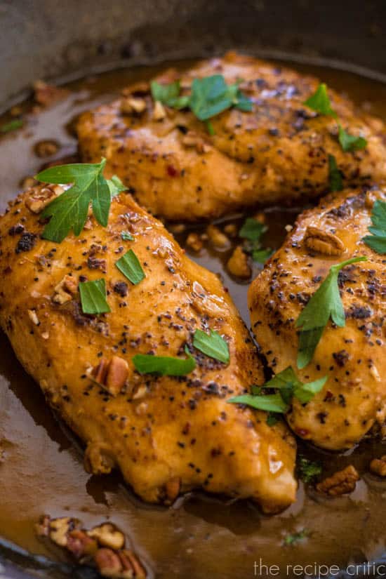 Cider glazed chicken simmering in a pan with green garnish.