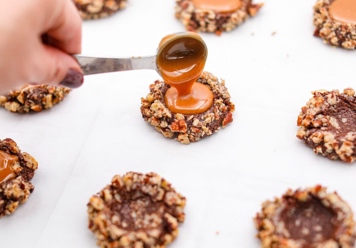 Angle shot of someone pouring the melted caramel into the indents in the baked cookies. 