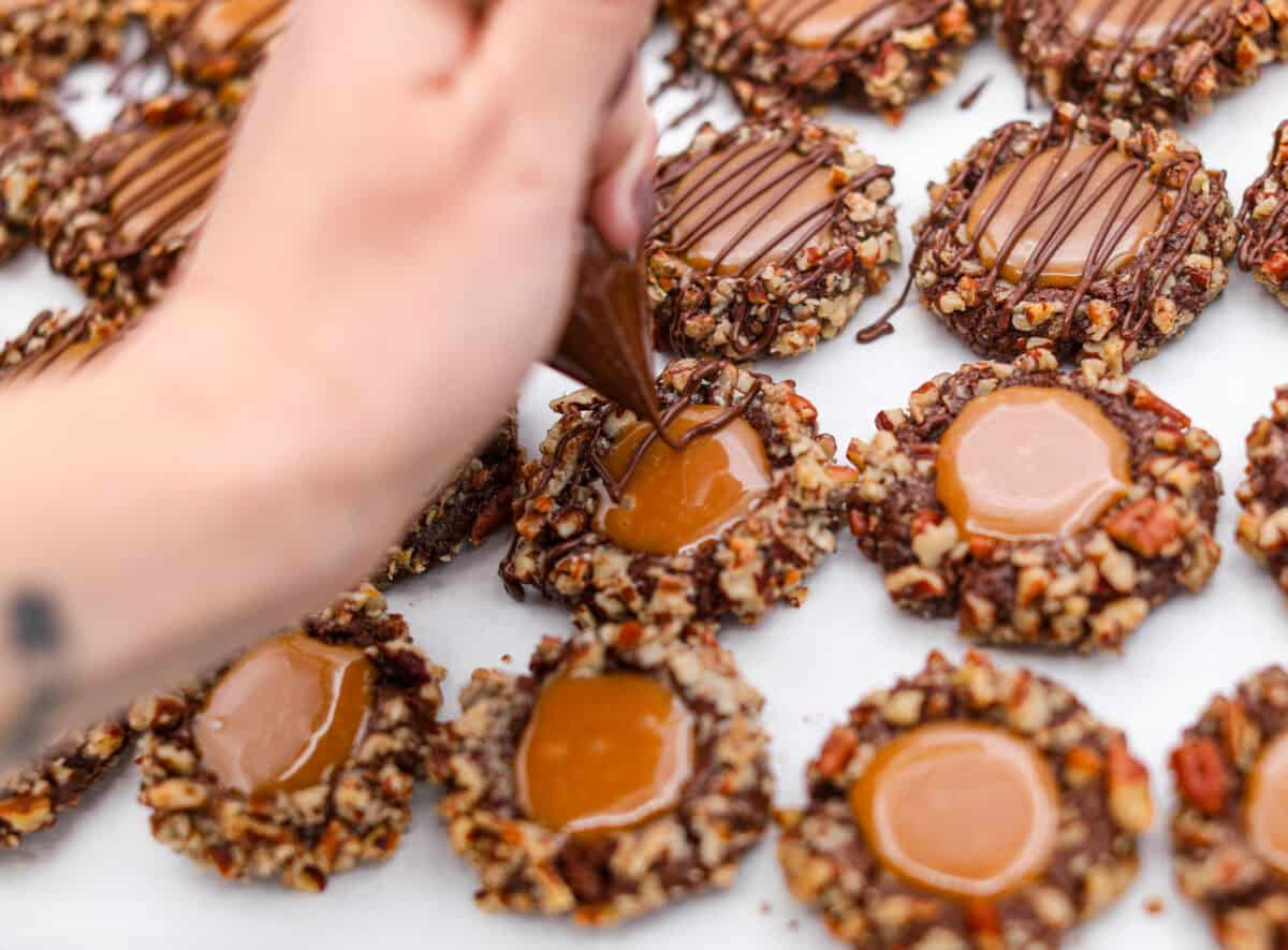 Close up shot of someone drizzling chocolate over the turtle cookies. 