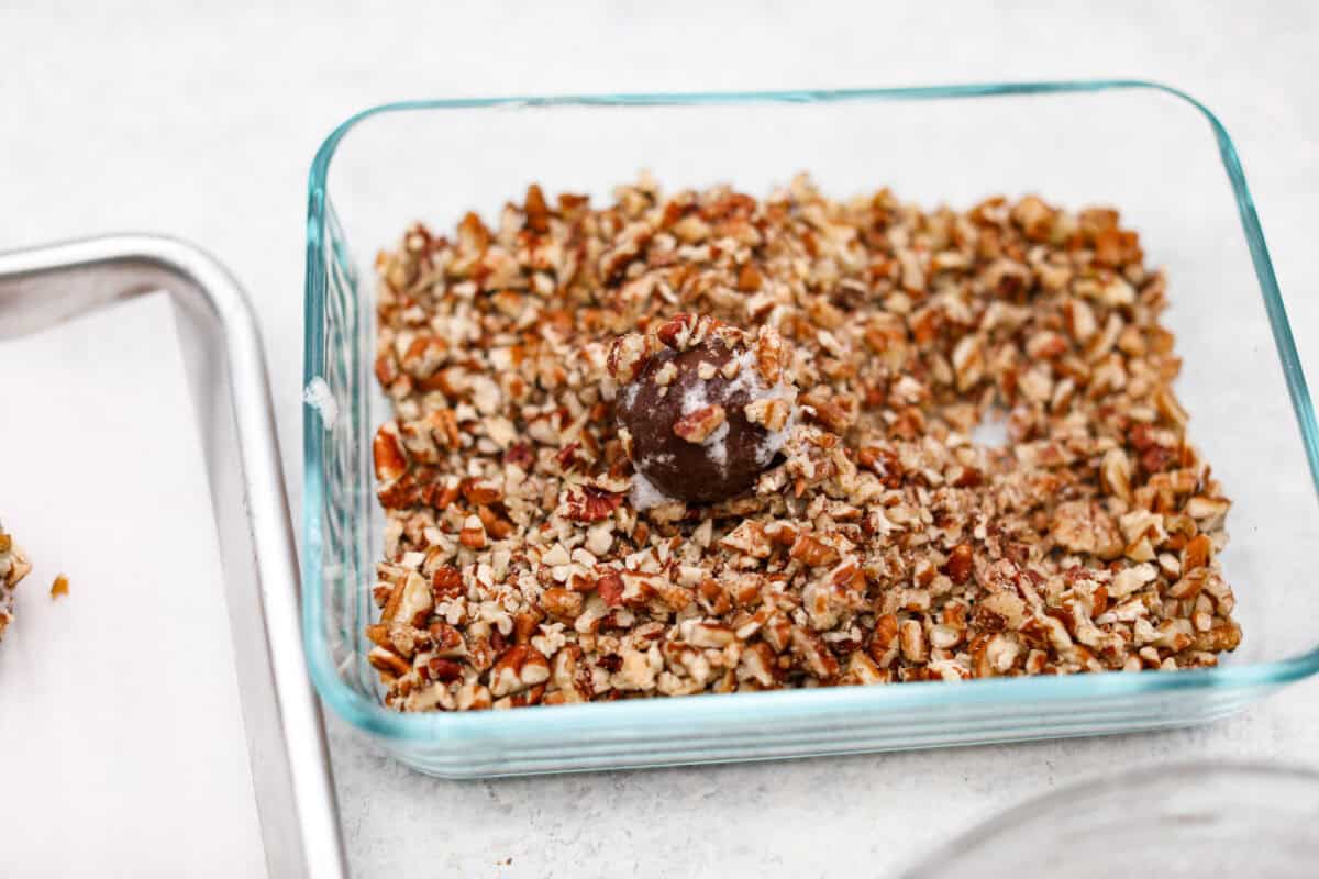 Angle shot of egg white coated dough ball in chopped pecans.