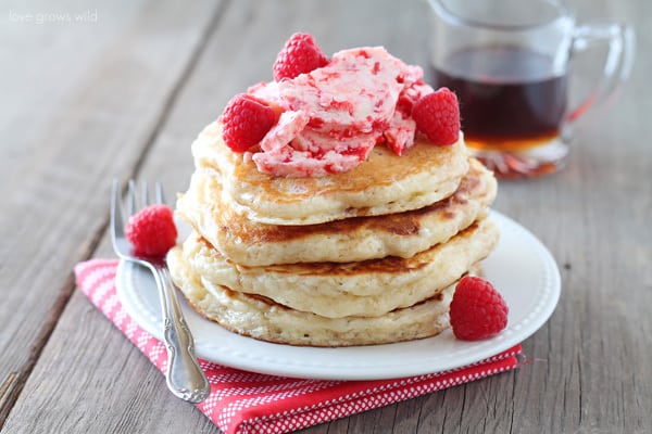 Raspberry butter on pancakes on a white plate with a metal fork on the side and syrup in the background. 