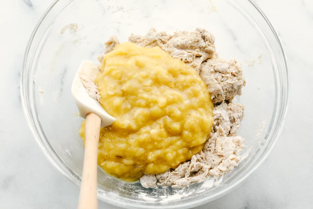 Banana mix in with ingredients in a glass bowl and spatula