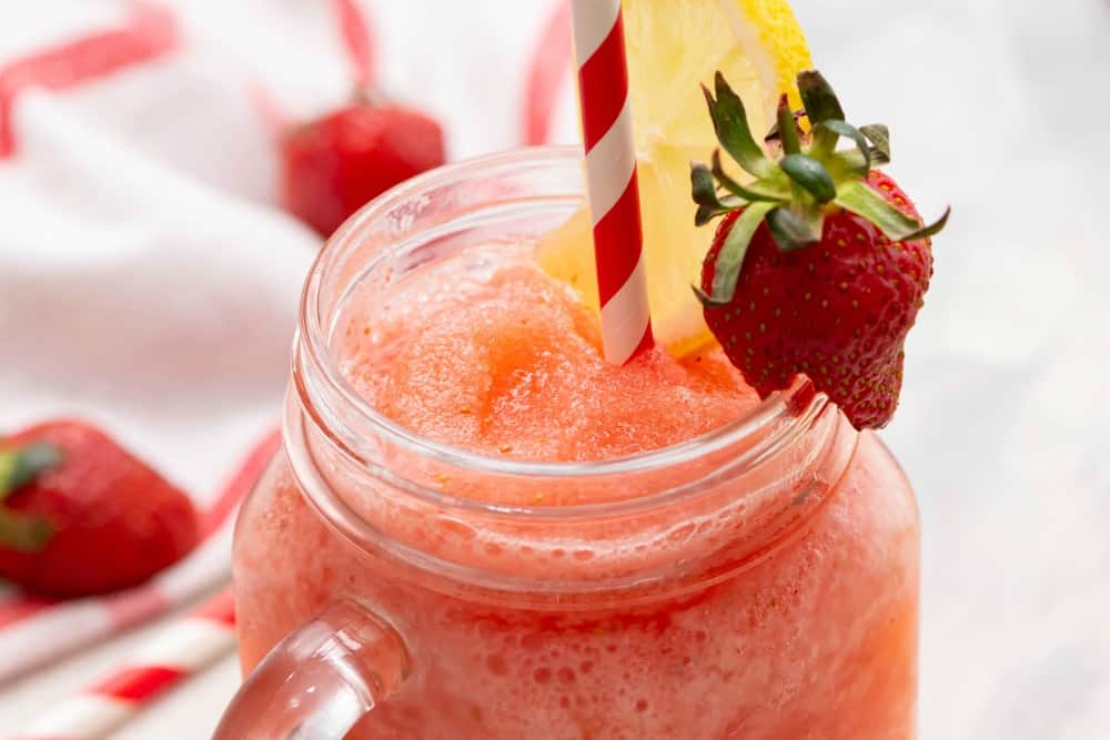 Frozen strawberry lemonade in a jar glass with a straw and strawberry on the side. 