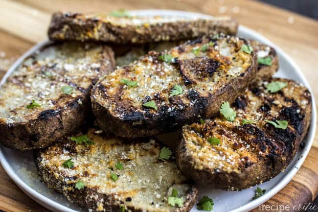 Grilled parmesan garlic potato planks stacked on top of each other on a white plate. 