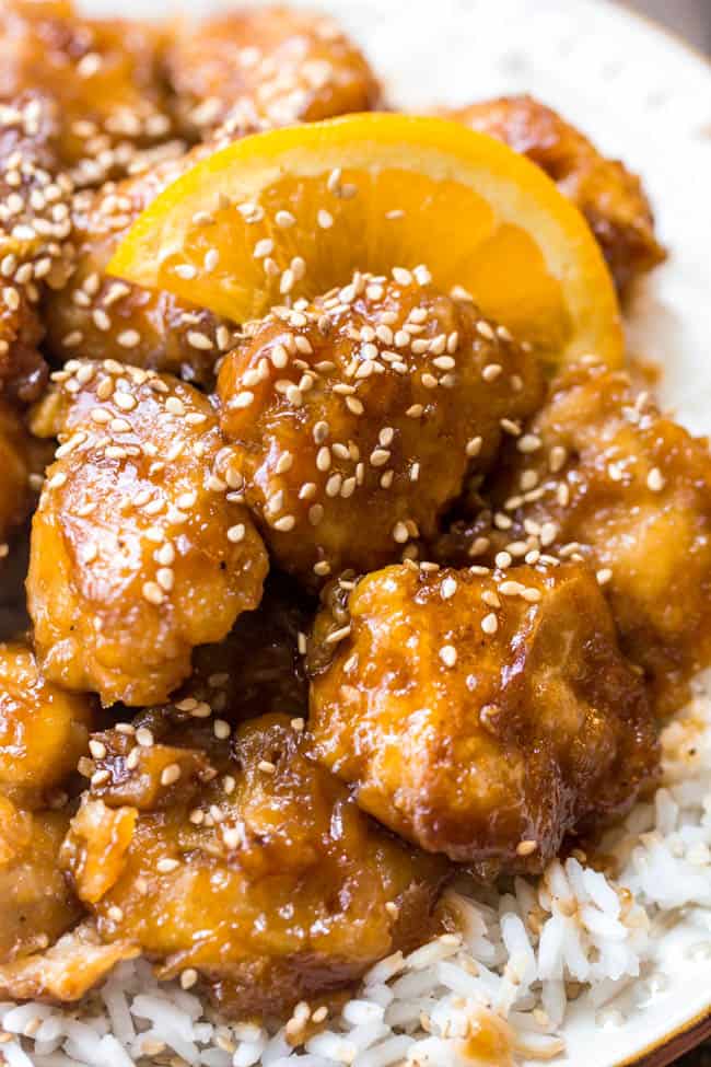 Orange chicken over rice with a slice of orange. 