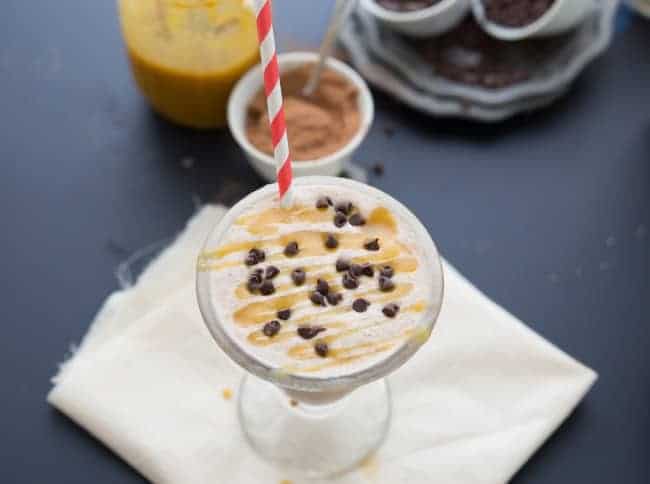 Overhead shot of milkshake with a straw in the drink glass and caramel with chocolate chips on top. 