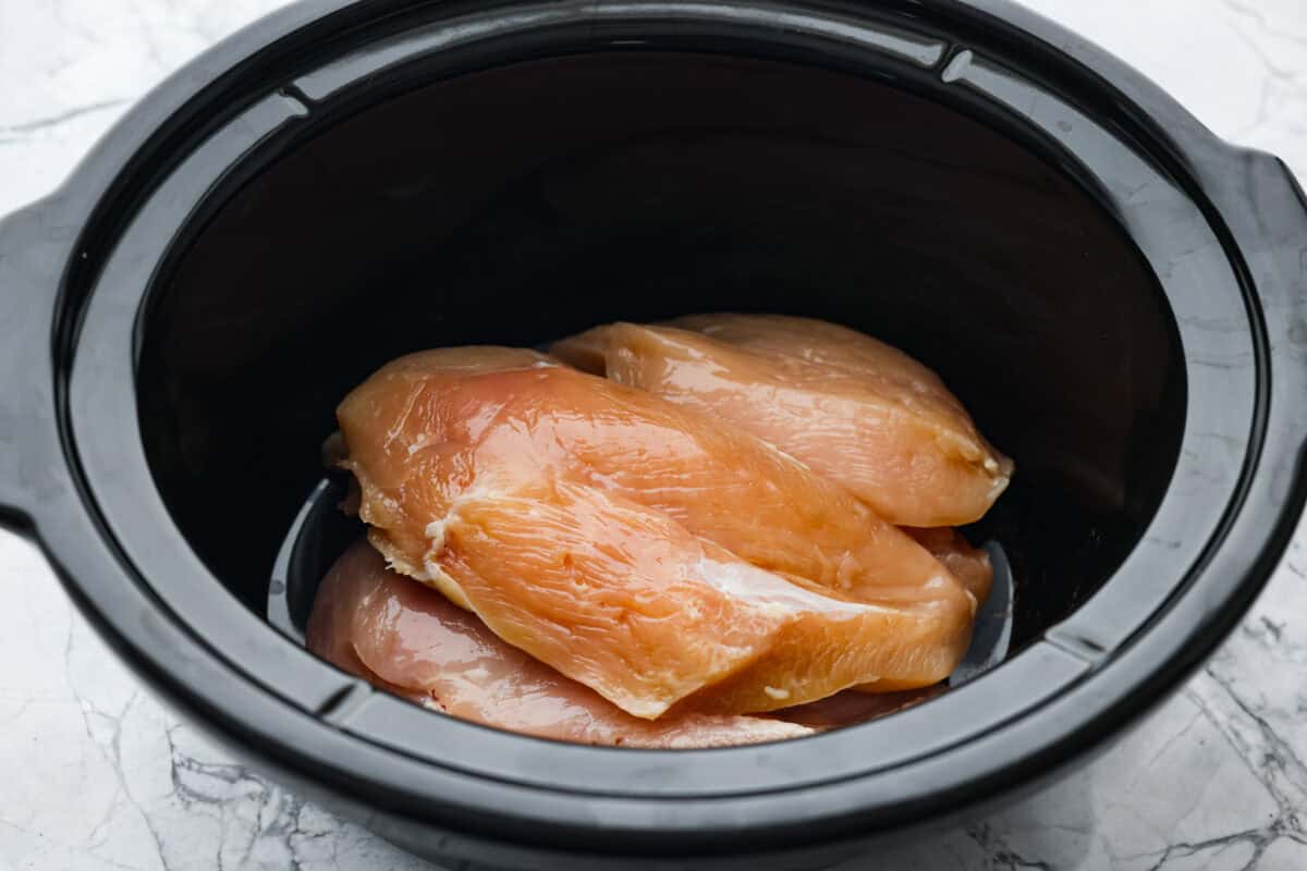 Overhead shot of chicken breasts in teh bottom of the slow cooker. 