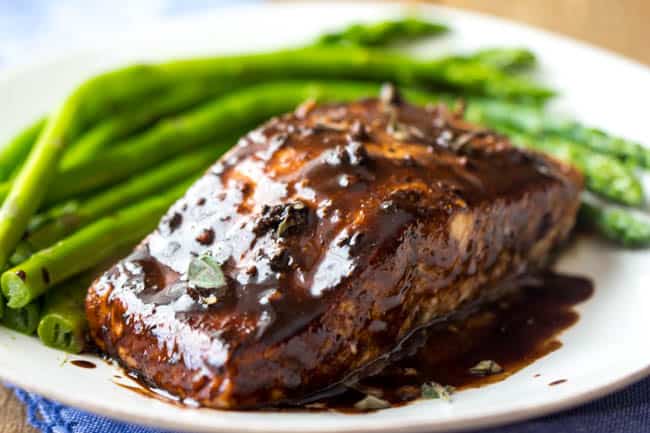 Honey balsamic glaze salmon on a white dish with asparagus on the side. 