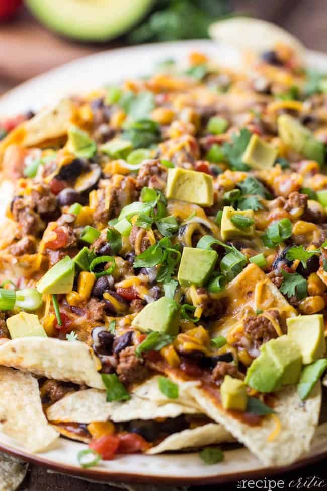 Beefy nachos stacked on top of each other on a white plate. 