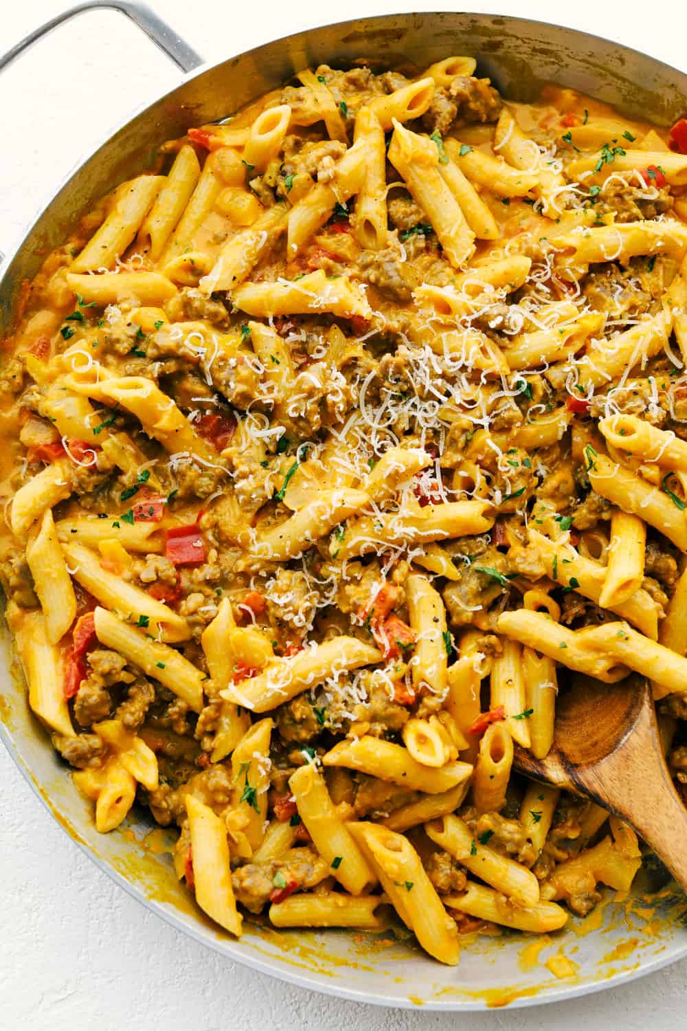 Sausage pumpkin pasta in a skillet with a wooden spoon stirring it. 