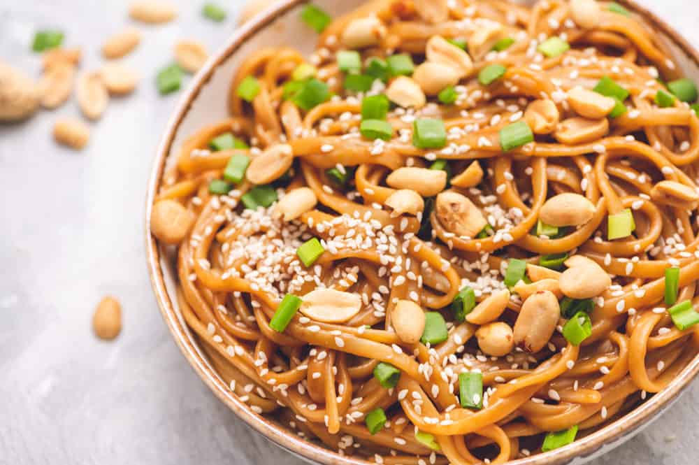 Thai peanut sesame noodles in a bowl with peanut halves garnished with scallops and sesame seeds.