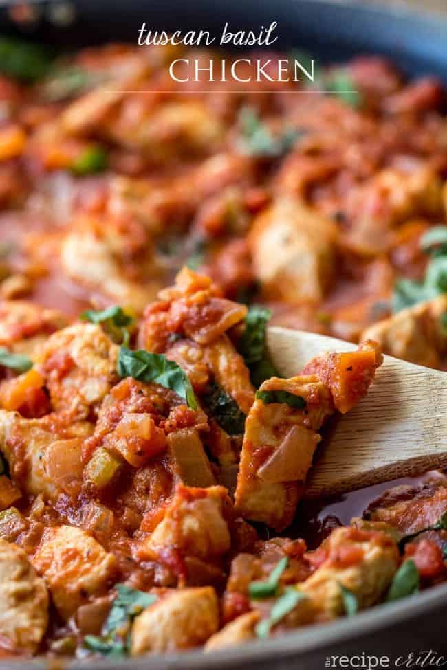 Tuscan basil chicken in a black skillet with a wooden spoon stirring it. 