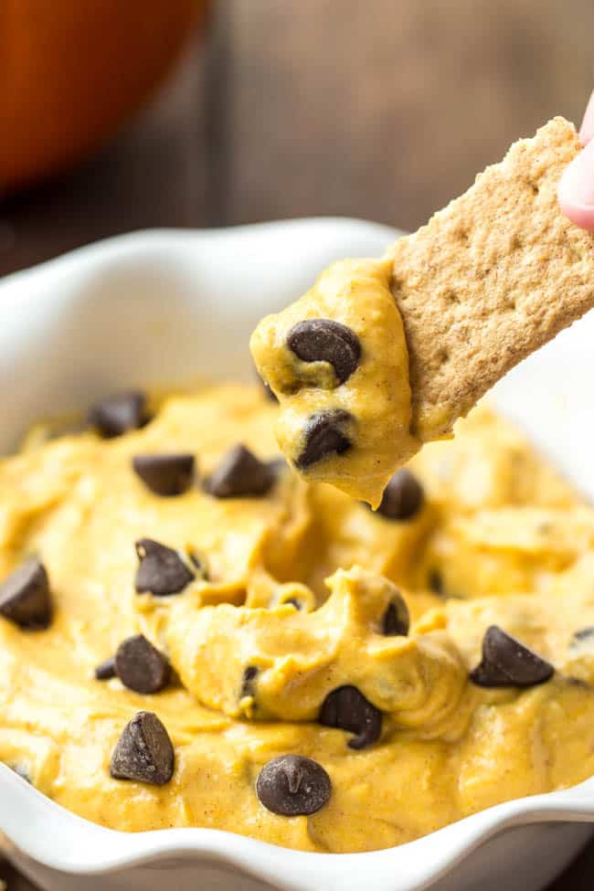 Pumpkin chocolate chip cookie dough being dipped in by graham crackers and garnished with chocolate chips. 