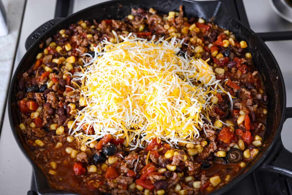 Overhead shot of meet and veggie mixture with cheese on top in a skillet. 