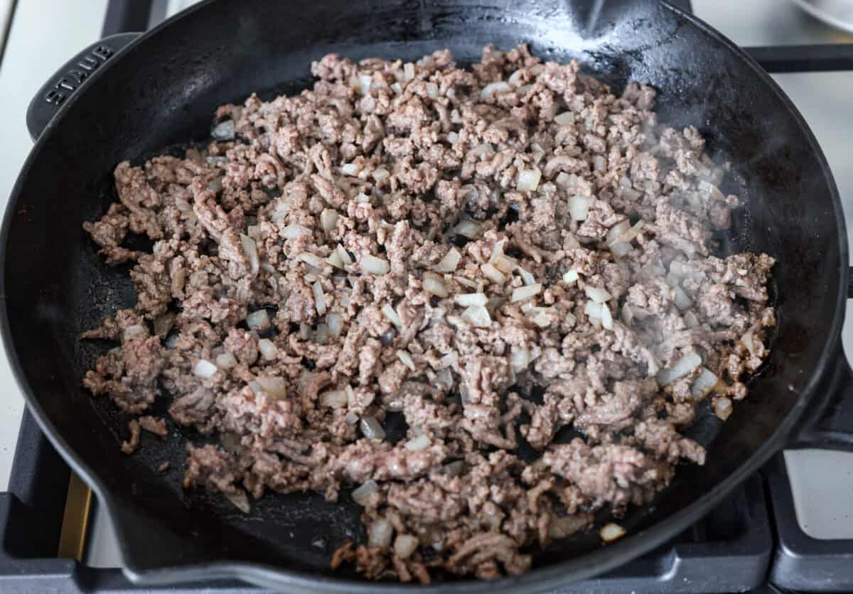 Angle shot of beef and onions sautéing in a skillet. 