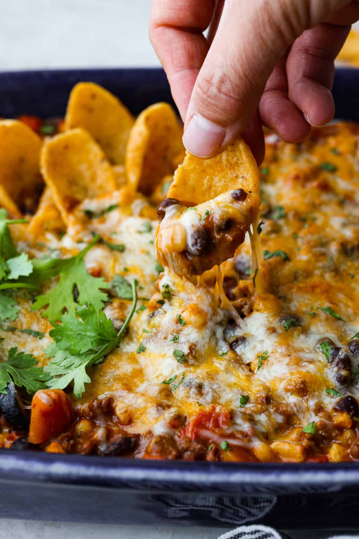 Side shot of someone dipping a chip into the beef enchilada dip. 