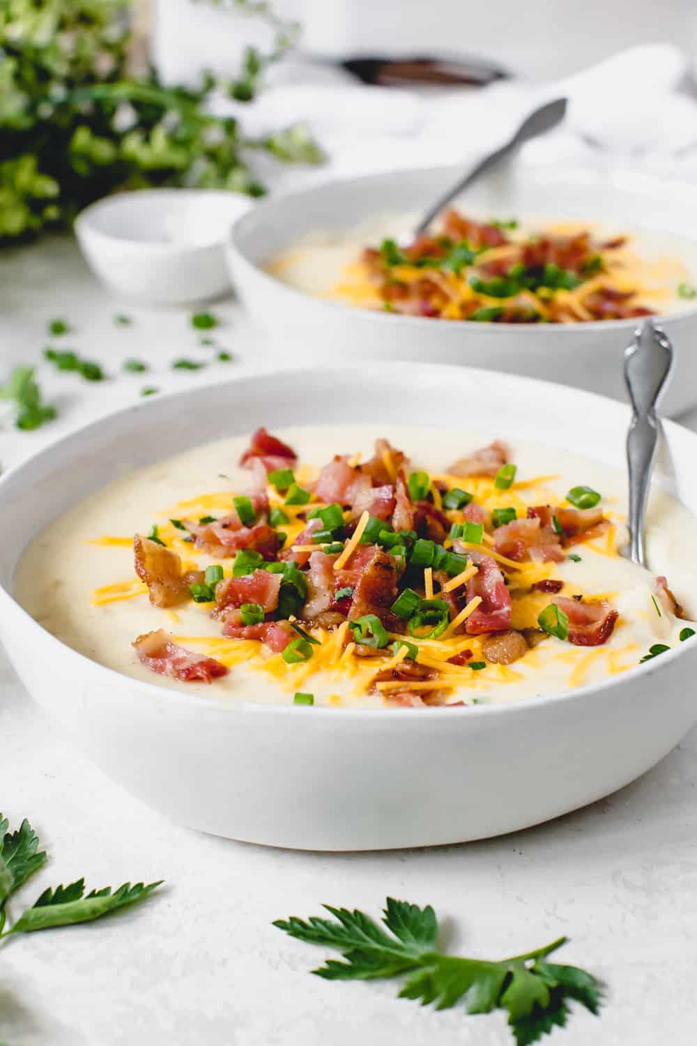 Two bowls full of loaded baked potato with a spoon garnished with chopped bacon, cheese and green onions. 