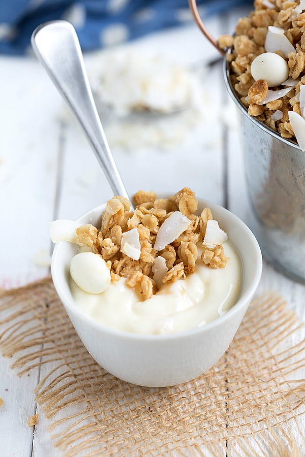 Tropical granola on top of a bowl of yogurt in a white cup with spoon.