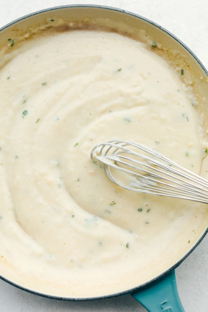 Top view of a whisk stirring the cream of chicken soup in a skillet.