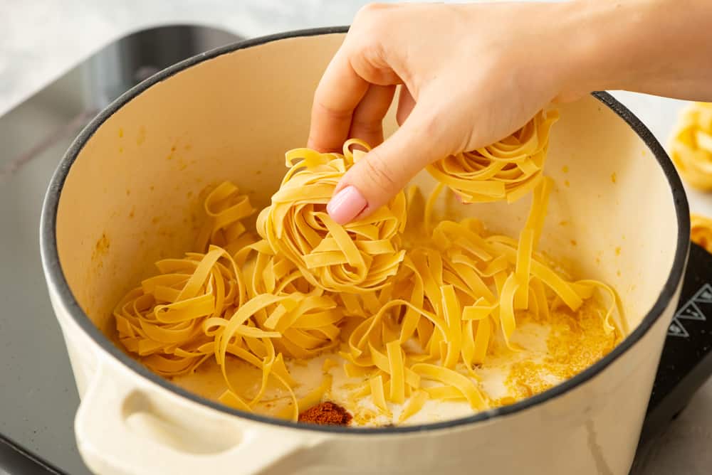 dried fettuccine noodles being added to the pot to cook